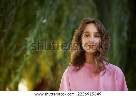 close-up portrait, beautiful young girl in a pink t-shirt, in the park. happy girl smiles and looks at the camera, the wind develops her hair.