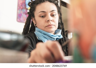 Closeup Portrait Of Beautiful Young White Girl Hispanic Latin Art Director, With Dreadlocks, Nice Eyes And A Blue Bandanna, In Her Art Studio Reaching Out To Grab Her Work Tool.