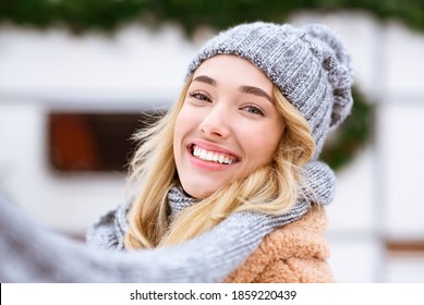 Closeup Portrait Of Beautiful Young Woman Posing Outdoors On Winter Day, Wearing Woolen Hat And Scarf, Cheerful Blonde Female Looking And Smiling At Camera, Selective Focus With Free Space - Powered by Shutterstock