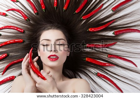 Closeup portrait of beautiful young woman lying on floor with chilli peppers in hair. Isolated over white background. Copy space.