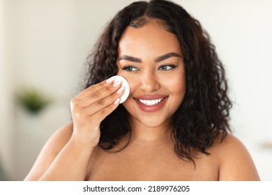 Closeup Portrait Of Black Plus Size Woman Using Cotton Pad, Erasing Make Up From Her Face, Applying Facial Toner Or Cleansing Milk, Bathroom Interior, Copy Space