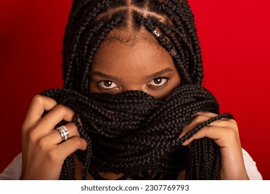Close-up portrait of black woman with holding her braids to her face. Isolated on red background