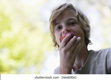 Closeup Portrait Of A Blond Boy Eating Apple Outdoors