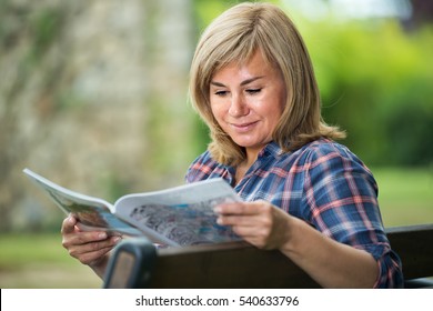 Closeup Portrait Of Blond Mature Woman Reading Magazine In Garden On Summer Day
