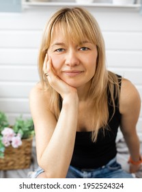 Close-up portrait of blonde, with bangs, landscape designer woman 40-42 years old, looks into the camera, hand under chin, without makeup. smile on face
