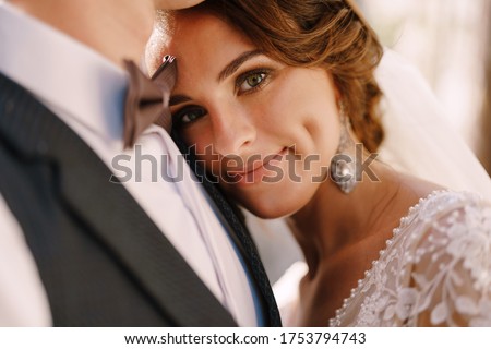 Close-up portrait of a bride looking at the camera, laid her head on the groom's chest. Beautiful wedding couple. Fine-art wedding photo in Montenegro, Perast.