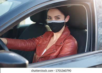 Closeup Portrait Of Brunette Female Driving Car, Woman Wearing Leather Jacket And Black Protective Mask, Lady Goes To Grocery Store Buying Convenience Food For Her Grandparents Which In Risk Group.