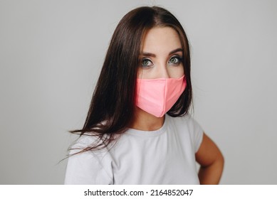 Closeup Portrait Of A Brunette Girl With Painted Eyes In A Mask Against A White Wall In Daylight. Respiratory Protection Concept