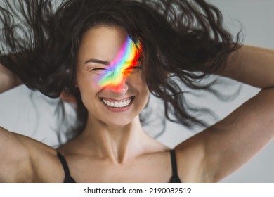 Closeup Portrait Of Brunette Girl Shaking Hair With Ray Of Rainbow Light On Her Face. Rainbow Flare On Woman Face. Art Beauty Portrait. Girl With Rainbow Shining Face Have Fun And Enjoying Life
