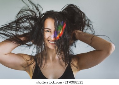 Closeup Portrait Of Brunette Girl Shaking Hair With Ray Of Rainbow Light On Her Face. Rainbow Flare On Woman Face. Art Beauty Portrait. Girl With Rainbow Shining Face Have Fun And Enjoying Life
