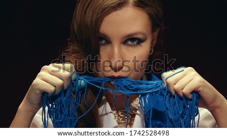 A close-up portrait of a brunette with long hair sitting at a table and eating blue spaghetti with her hands. Creative photo session. Italian food or cooking concept.