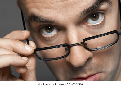 Closeup portrait of a businessman with hand on glasses making a face against gray background