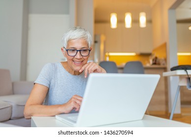 Close-up portrait of casual woman using her laptop while sitting on couch and working. An attractive middle aged businesswoman sitting in front of laptop and managing her small business from home. - Powered by Shutterstock