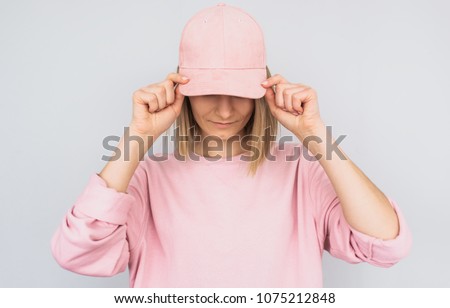 Closeup portrait of Caucasian blonde young female wearing pink sweater and cover her eyes with pink cap, protect from the sun rays, isolated on white studio background. Positive people emotion concept