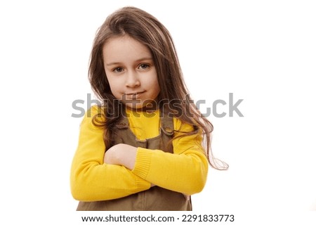 Close-up portrait of Caucasian child 5-6 years old, adorable little girl confidently looking at camera, posing with hers arms folded over white isolated background with free advertising space