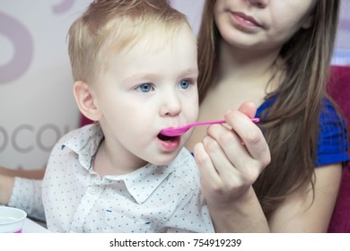 close-up portrait of a caucasian kid boy with a big blue eyes, which his mother with a spoon is feeding ice cream in a cafe