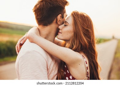 Close-up portrait of a caucasian young loving couple embracing while standing on a roadside. Couple embracing road travel. Sunset scene. - Shutterstock ID 2112812204