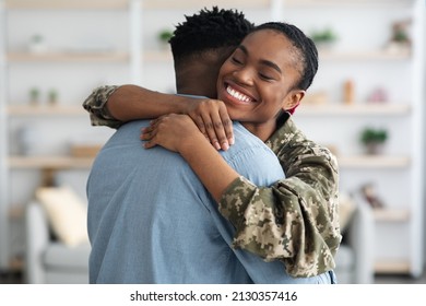 Closeup portrait of cheerful black female soldier lady in camouflage uniform hugging her boyfriend, home interior. Military wife came back from army, embracing her loving husband, finally together - Shutterstock ID 2130357416