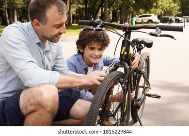 Closeup Portrait Of Cheerful Dad And Son Fixing Bike Using Wire Cutter At Public Park