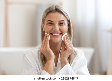 Closeup Portrait Of Cheerful Middle Aged Woman With Blonde Hair Using Cotton Pads, Erasing Make Up From Her Face, Applying Facial Toner Or Cleansing Milk, Bathroom Interior, Copy Space