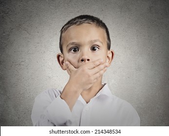 Closeup Portrait Child Astonished Face Expression, Covering Mouth With Hand, Wide Open Eyes, Isolated Grey Wall Background. Human Emotions, Body Language, Perception. Unexpected Discovery, Reaction