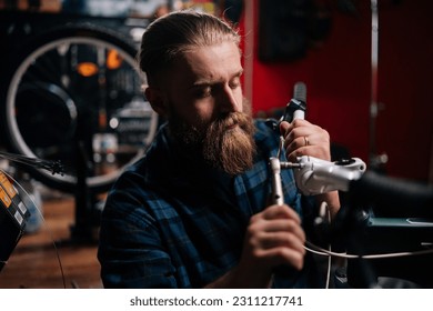 Closeup portrait of concentrated cycling mechanic male checking and repairing bicycle handlebar with special tools working in bike repair shop with dark interior. Concept of maintenance of bike.