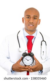 Closeup Portrait Of A Concerned, Serious, Busy, Confident Male Doctor Holding An Alarm Clock Running Out Of Time Isolated On A White Background. Health Care Reform, Medicaid Reimbursement.