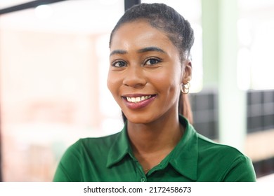 Close-up Portrait Of Confident African-american Female Employee Standing In Modern Office Space, Cheerful Attractive Black Businesswoman In Green Shirt Looks At The Camera With Light Friendly Smile