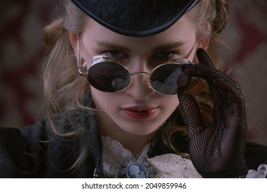 Close-up portrait of a confident elegant lady in a 19th century suit looking over her round glasses. Historical hairstyle and makeup. Steampunk lady.