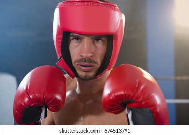 Close-up portrait of confident male boxer wearing red headgear and gloves in boxing ring - Powered by Shutterstock