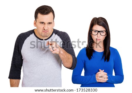 Closeup portrait of couple. Bully husband, man standing upfront, angry, pointing at you and shy wife, nerdy woman wearing glasses standing behind him, isolated on white background. Human emotions
