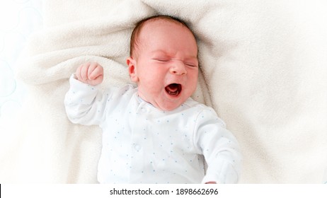 Closeup Portrait Of Crying Newborn Baby Lying In Baby Crib.