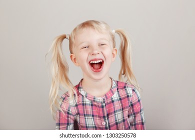 Closeup Portrait Of Cute Adorable White Blonde Caucasian Preschool Girl Smiling In Front Of Camera In Studio. Child Laughing Posing On Plain Light Background. Kid Expressing Emotions