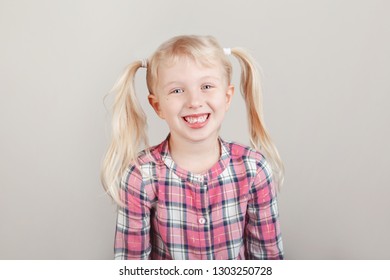 Closeup Portrait Of Cute Adorable White Blonde Caucasian Preschool Girl Smiling In Front Of Camera In Studio. Child Laughing Posing On Plain Light Background. Kid Expressing Emotions