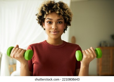 Closeup Portrait Of Cute African American Female With Afro Hair Holding Green Dumbbells Doing Training Workout At Home, Building Muscles, Wearing Red T-shirt. Healthy Lifestyle, Fitness At Home