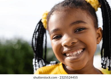 Close-up portrait of cute african american girl smiling at camera against clear sky in yard. Unaltered, childhood, face, happy and lifestyle concept.
