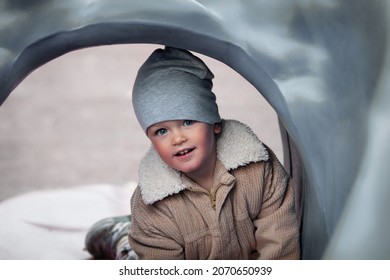 Close-up portrait of cute baby boy in beanie and jacket looking and smiling at camera. Child on gray playground outdoors - Powered by Shutterstock