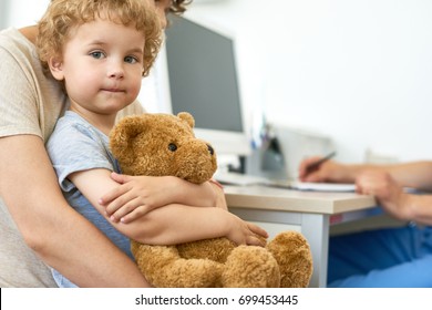 Closeup Portrait Of Cute Child Sitting On Mothers Lap In Doctors Office Waiting For Check Up Hugging Plush Teddy Bear Toy