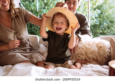 Closeup Portrait Of Cute Kid, Small Boy Wearing Straw Hat Sit With Parents In Cozy Bedroom Or Rv Van With Big Window Over Green Summer Forest. Young Lovely Family Have Fun Together On Camper Road Trip