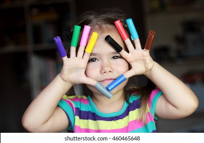 Close-up portrait of cute smiling girl with colorful cap of markers on her fingers, education and school concept