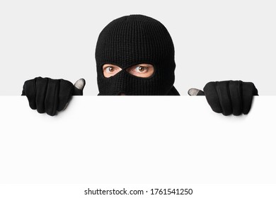 Closeup portrait of disguised looter peeping out white blank advert billboard, isolated over white studio background
