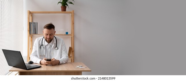 Close-up Portrait Of A Doctor He Uses A Mobile Smartphone, Works On A Laptop In A Medical Office In A Hospital, EHR Electronic Medical Record System, Cloud Storage Technology Concept. Copy Space.