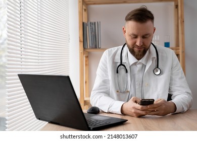 Close-up Portrait Of A Doctor He Uses A Mobile Smartphone, Works On A Laptop In A Medical Office In A Hospital, EHR Electronic Medical Record System, Cloud Storage Technology Concept.