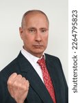 closeup portrait of elderly man in dark suit and red tie in style of Russian President Putin shows his fist against light background, concept Vladimir Putin