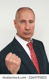 closeup portrait of elderly man in dark suit and red tie in style of Russian President Putin shows his fist against light background, concept Vladimir Putin's doubles, politics, economic sanctions