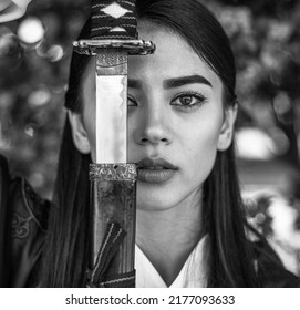 Close-up portrait of an elegant girl lady in the form of a samurai with a steel sword katana female prowess and courage in a penetrating look, black and white photo
