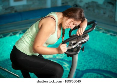 Closeup portrait of exhausted brunette woman riding exercise bike at fitness club
