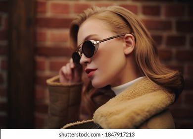 Close-up Portrait Of A Fashionable Young Woman In Modern Sunglasses Over Brick Wall Backgroud. Winter Style. Beauty, Fashion Concept. Optics, Eyewear.