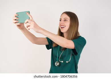 Close-up Portrait  Female Doctor Wearing A Green Scrubs And Stethoscope Is On White Background Taking A Selfie To Post It On Social Media Or Having A Video Call With Friends.