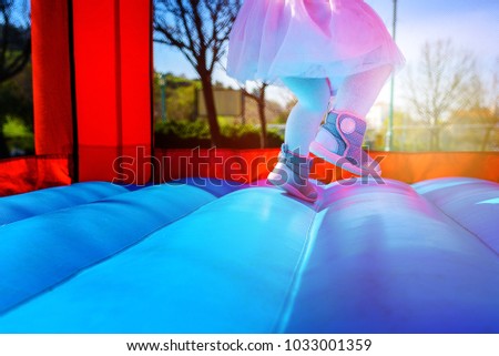 Close-up portrait of female joyful little girl legs jumps on a big inflatable trampoline outdoors in the park.
